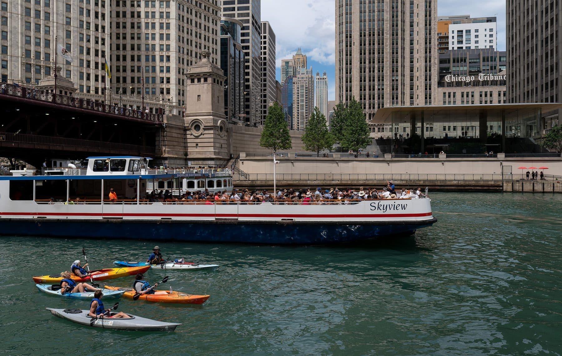 A Chicago river tour boat full of passengers passing the Tribune Tower, with kayaks in the foreground.